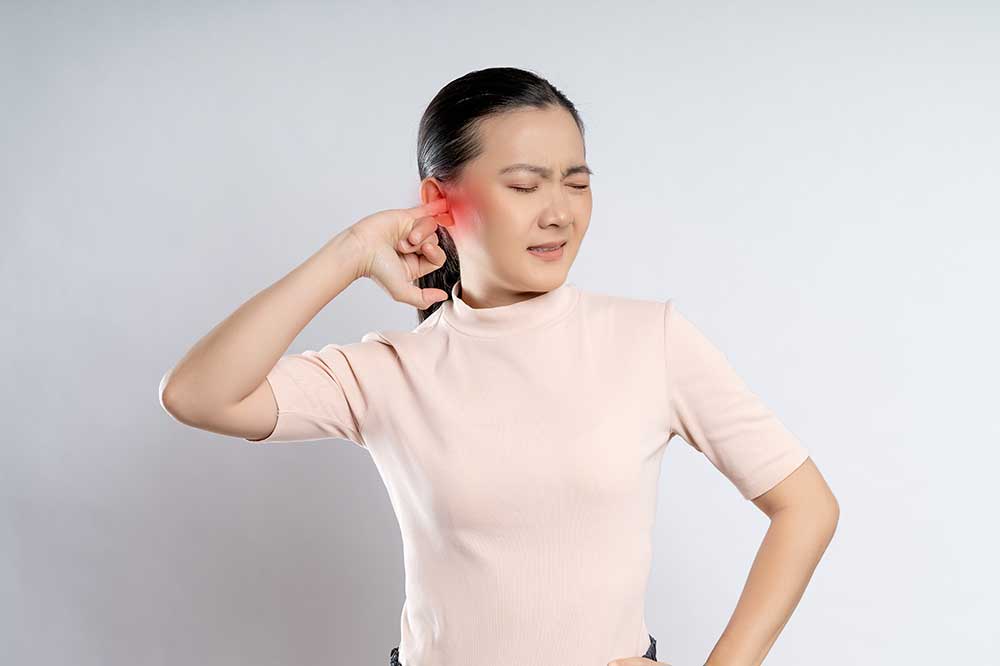 Woman wincing as she presses a finger into a sore, clogged ear, a concern Lexington Hearing and Speech Center sees in East Elmhurst, NY
